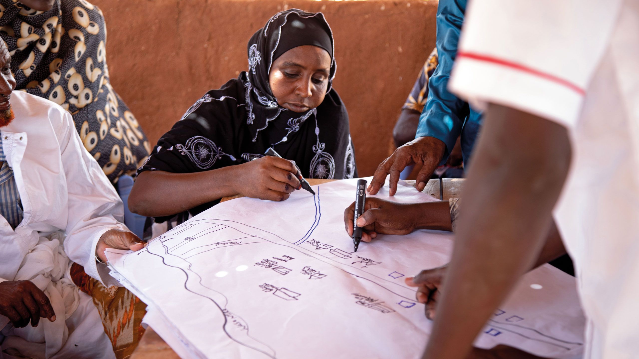 Ms. A. Wajera. from Biliqo village, northern Kenya, draws on village risk map she is preparing with the DRR committee in her community